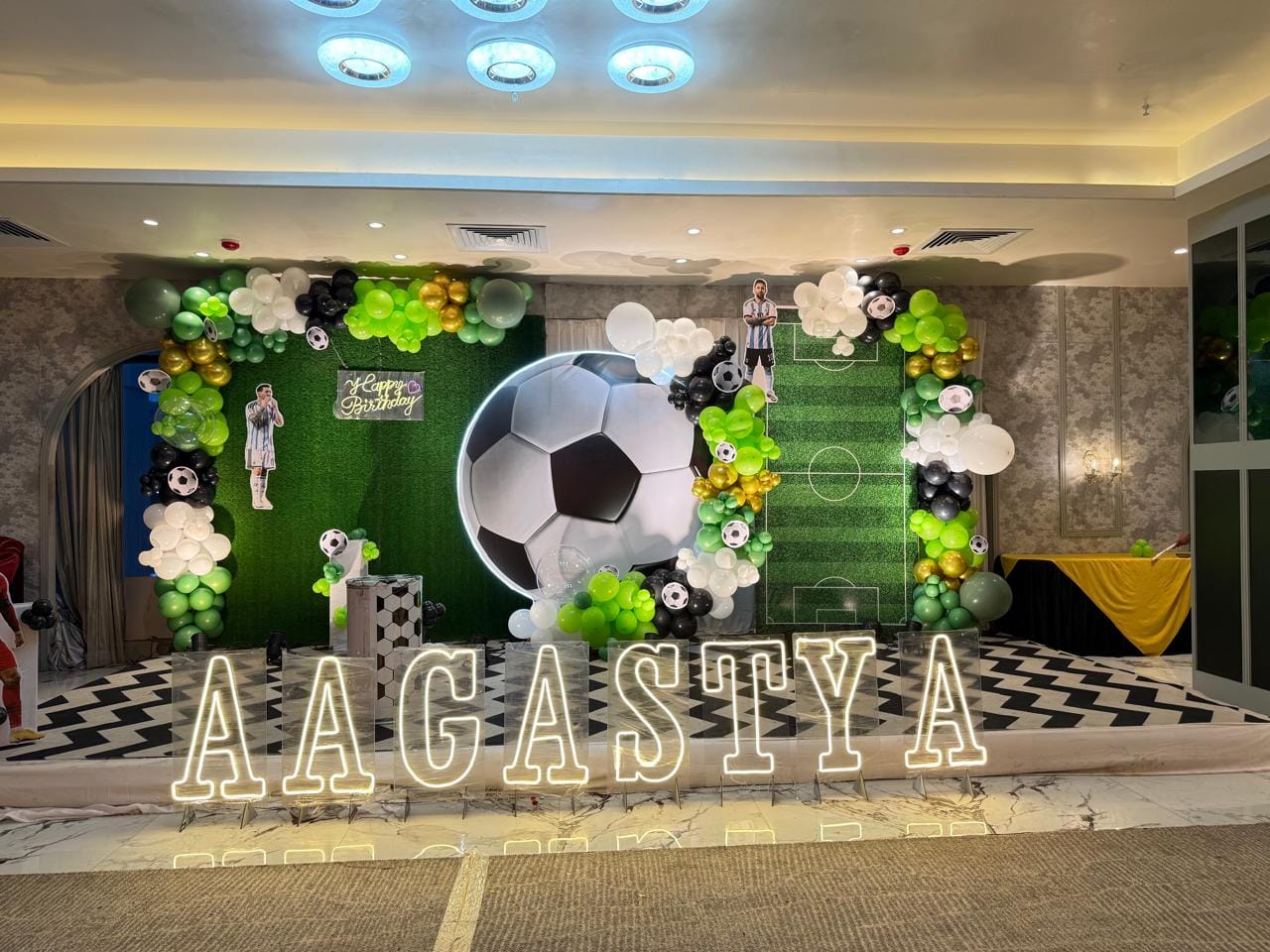 Football-themed birthday stage with a giant soccer ball, green field backdrop and an AAGASTYA name sign
