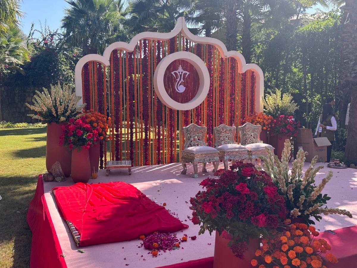 Haldi stage with Ganesh motif backdrop, marigold strings and red-pink floral styling