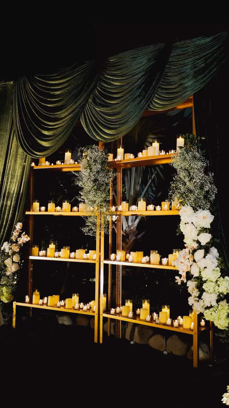 Golden open shelving filled with candles and white floral arrangements against dark green drapes