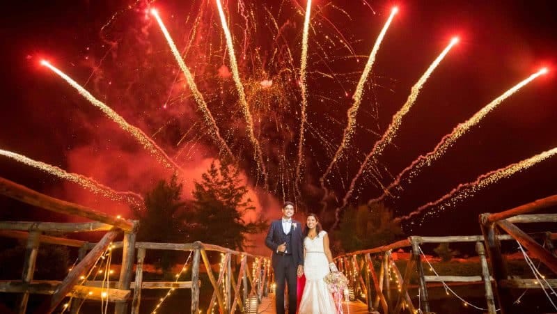 Wedding couple on a wooden walkway beneath red and golden fireworks