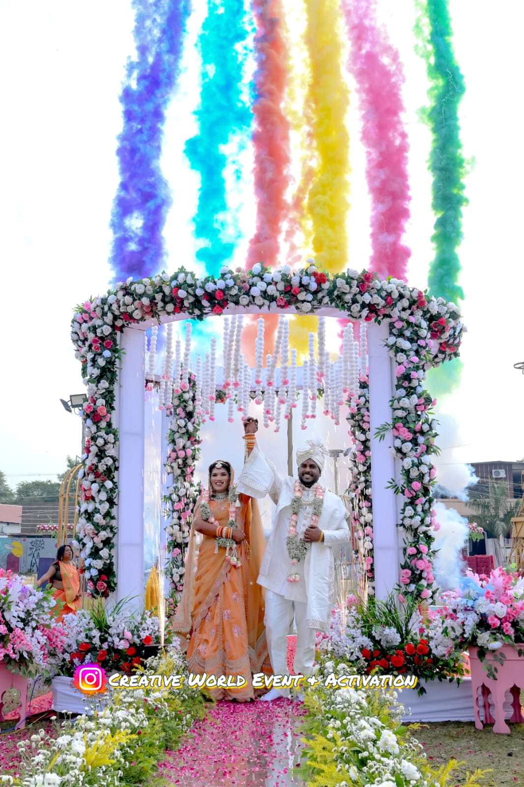 Couple under a floral entry arch with rainbow colour smoke rising behind them