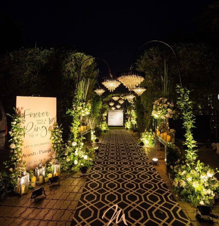 Night-time wedding entrance with a patterned walkway, illuminated welcome sign and floral greenery