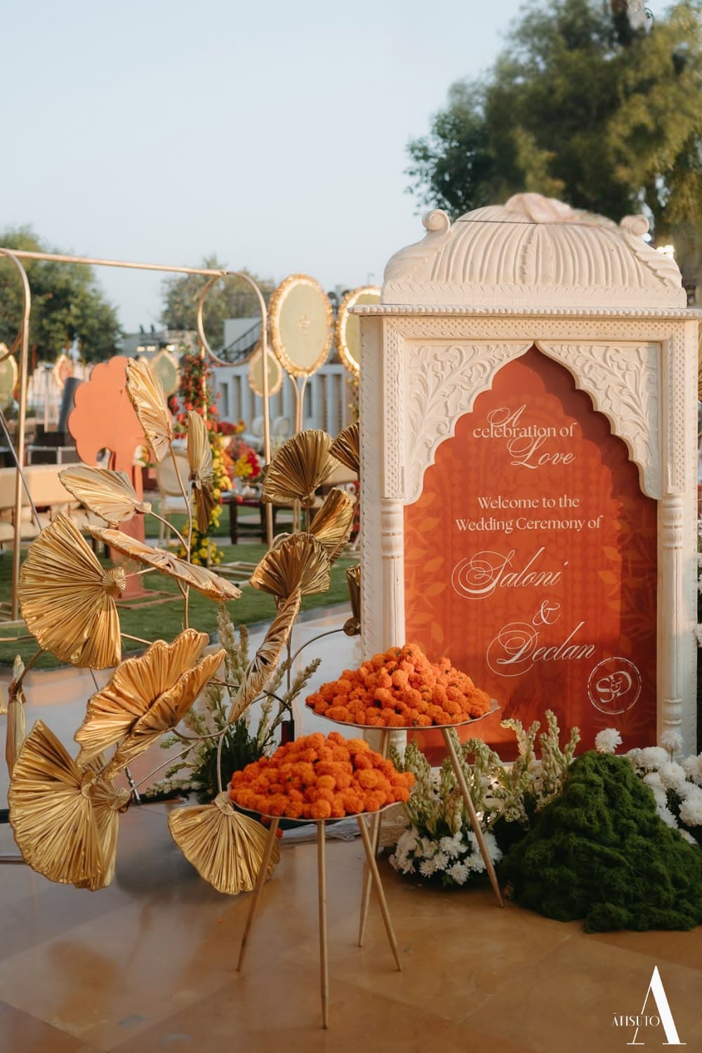Ornate white and rust-coloured welcome sign styled with orange flowers and gold leaf decorations