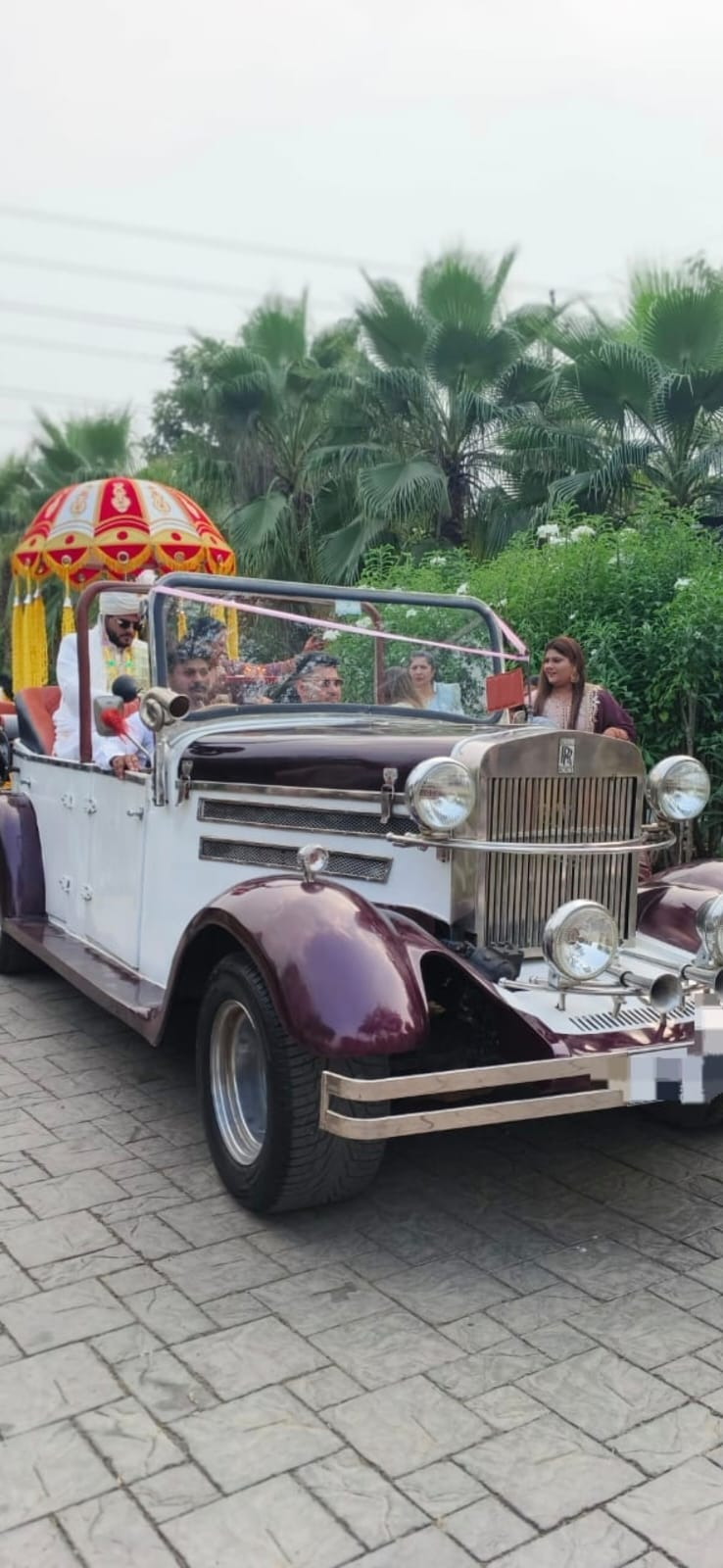 Purple and cream vintage car with an umbrella canopy carrying the couple