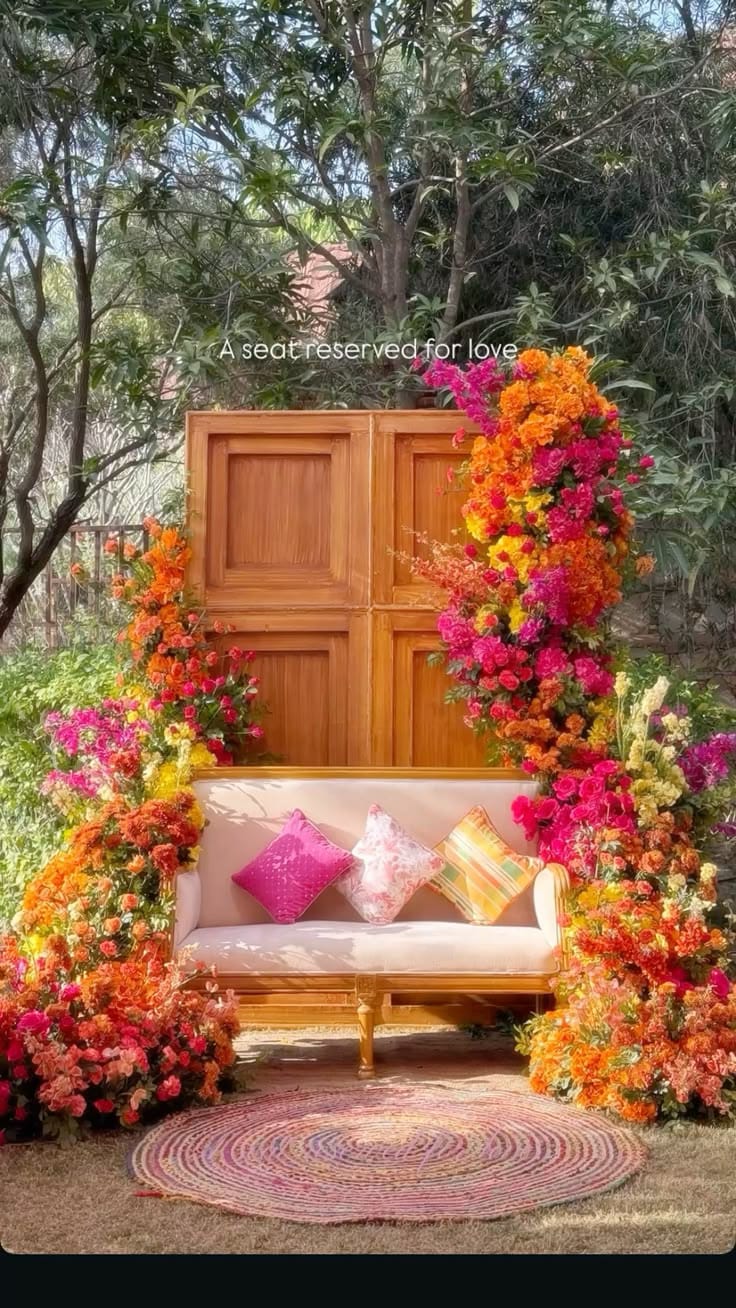 Wooden door photo booth framed with orange and pink bougainvillea and a cushioned bench