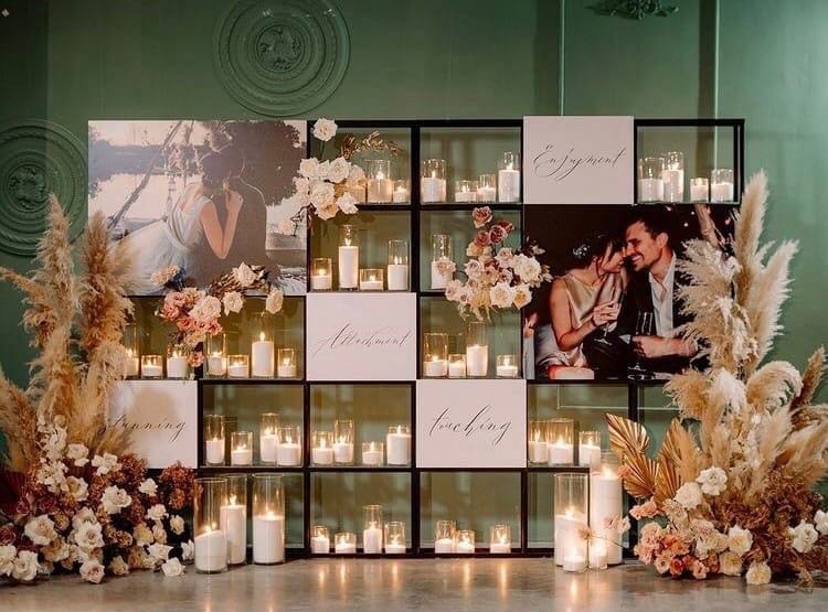 Photo display backdrop styled with pampas grass, pastel flowers, candles and framed celebration photographs