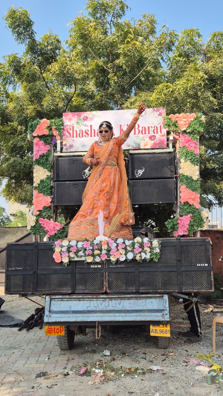 Dancer in an orange lehenga performing on a flower-decorated baraat truck