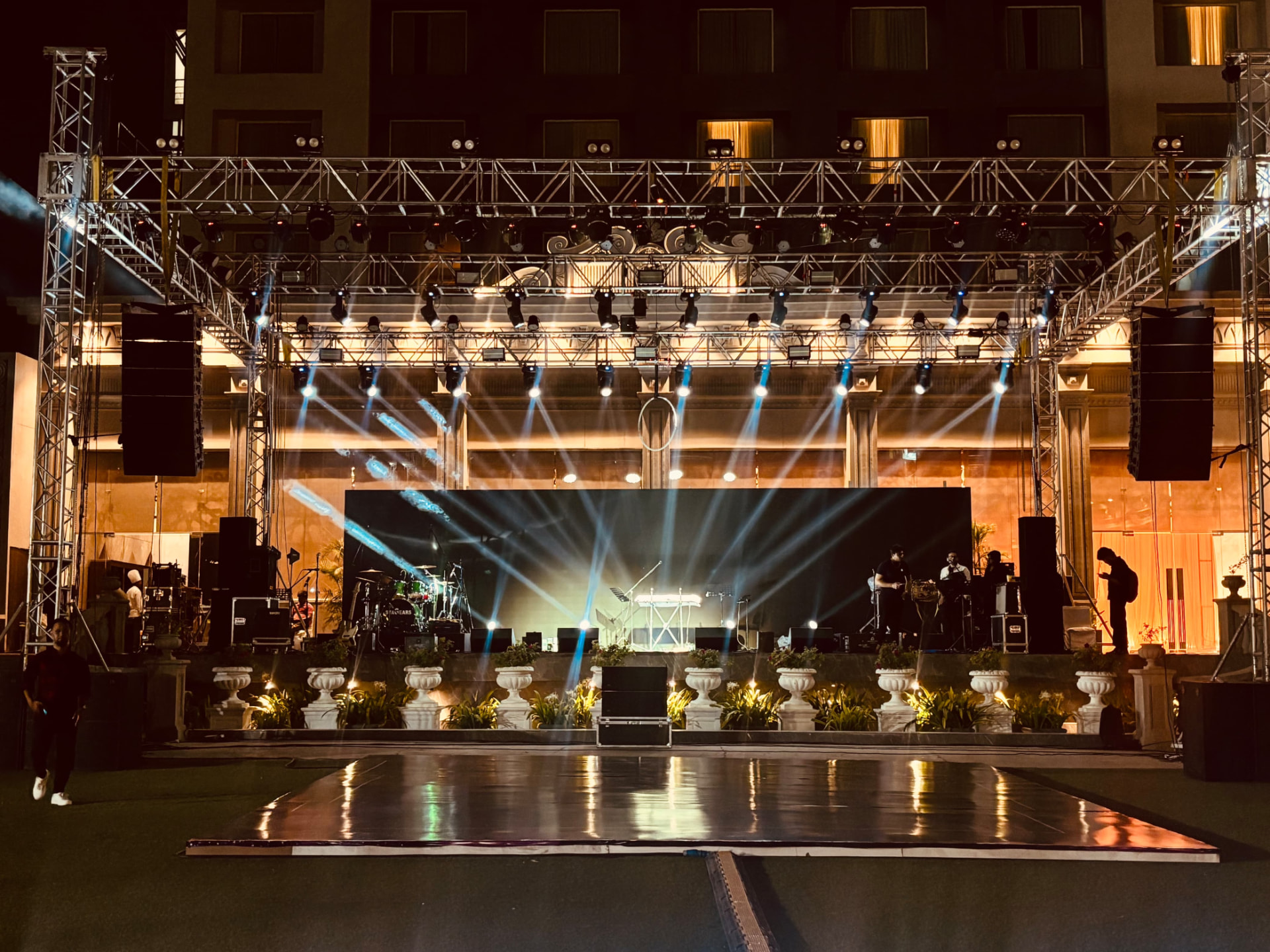 Sangeet stage with overhead lighting trusses, suspended speakers and a reflective dance floor