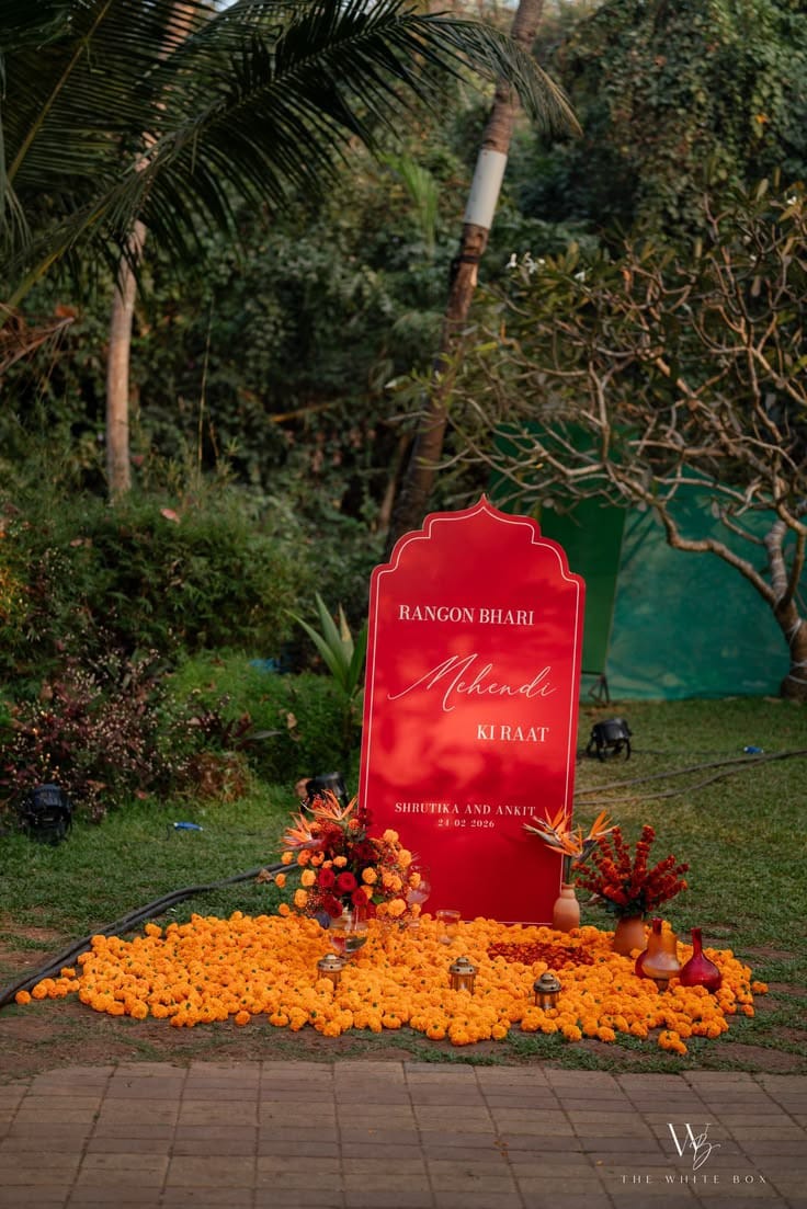 Red welcome sign with orange marigold arrangements beside a tropical garden pathway