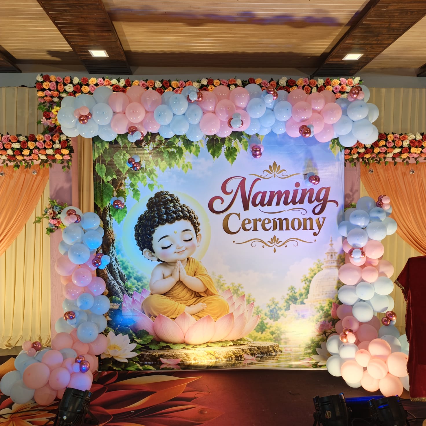 Naming ceremony backdrop with a Buddha motif, pastel balloon garland and floral accents