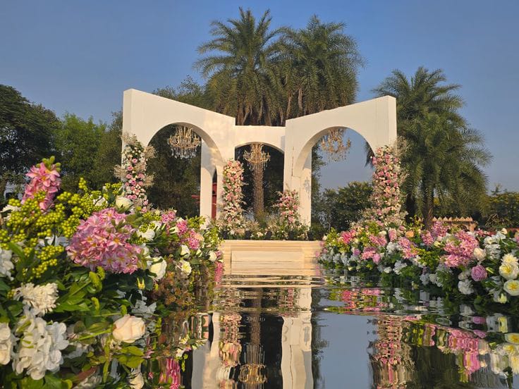 White arched mandap set beside a reflecting pool with lush pink and white florals