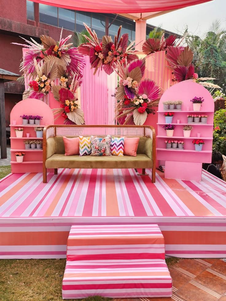 Pink striped celebration stage with a sofa, arched shelves and bright tropical floral arrangements