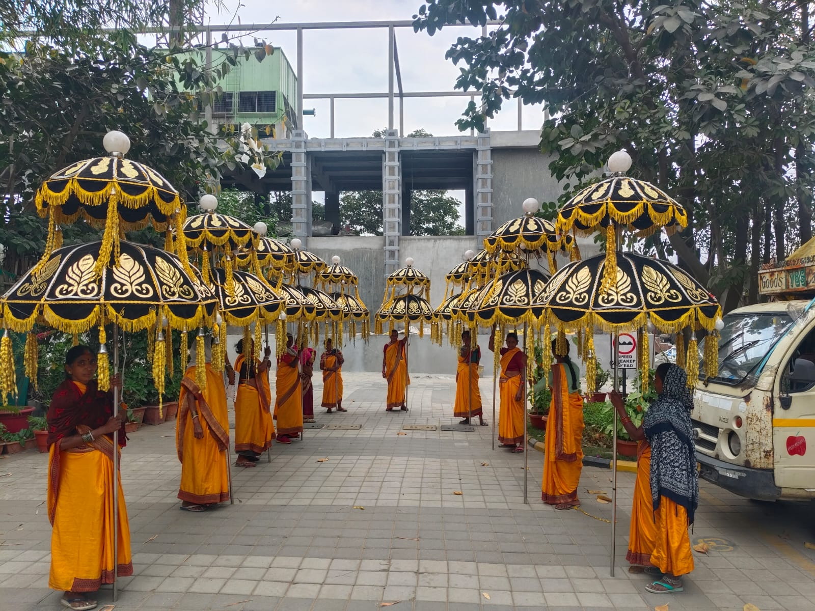 Attendants in orange attire carrying traditional golden embroidered baraat umbrellas