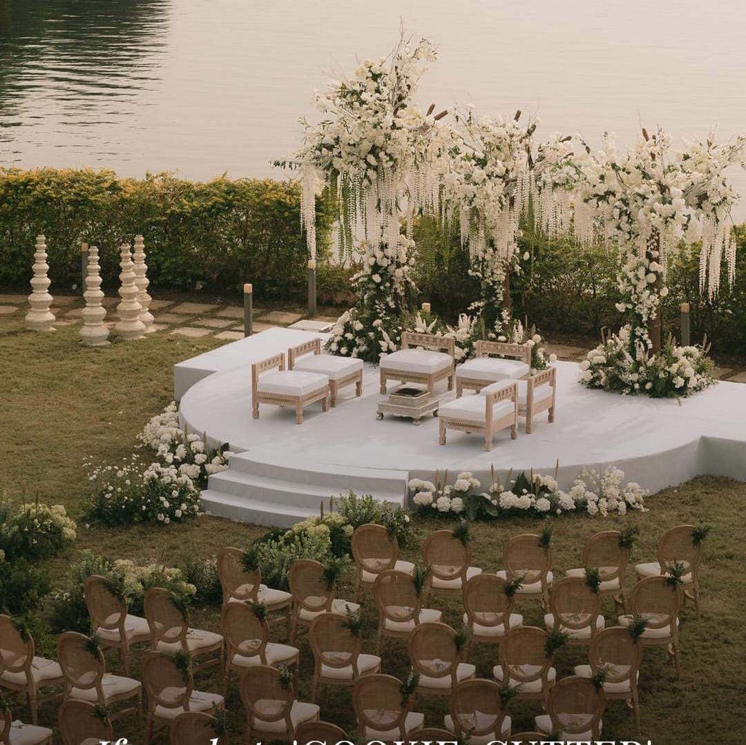 Round white waterfront ceremony stage with floral arches, seating and rows of guest chairs on the lawn