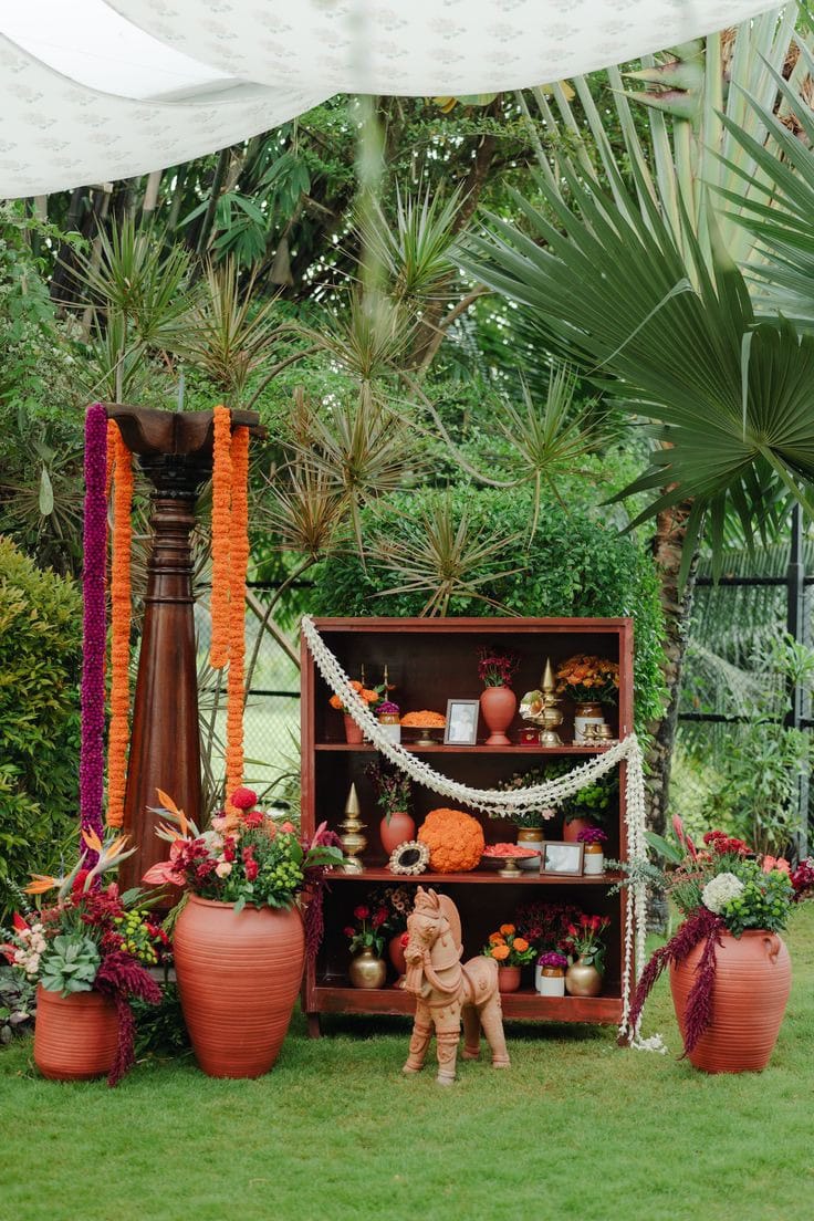 Garden display of terracotta pots and decorative objects with marigold garlands, tropical leaves and flowers