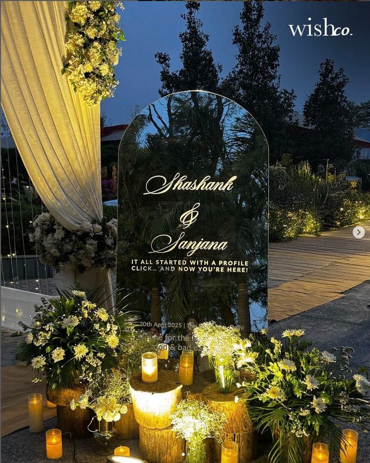 Mirrored wedding welcome sign beside yellow drapes, white-yellow flowers and glowing lanterns