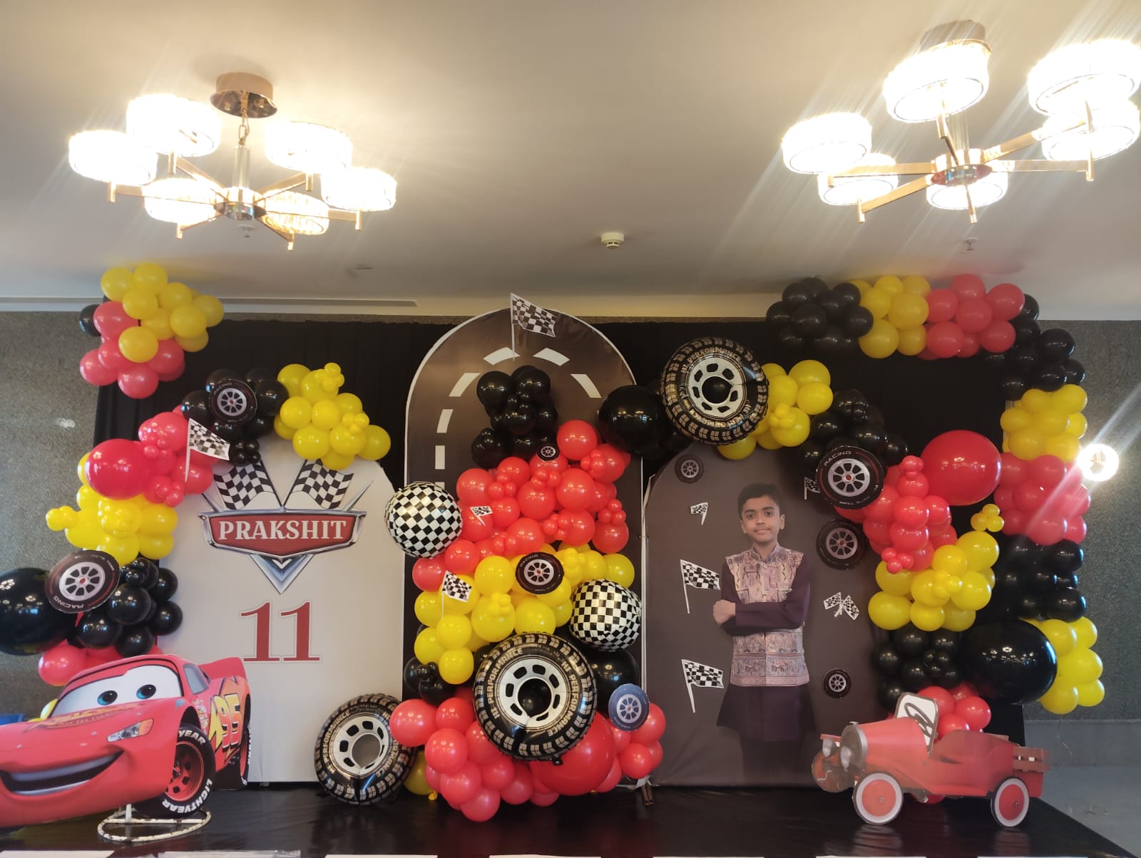 Race-car themed first birthday stage with red balloons, checkered backdrop and car cutouts